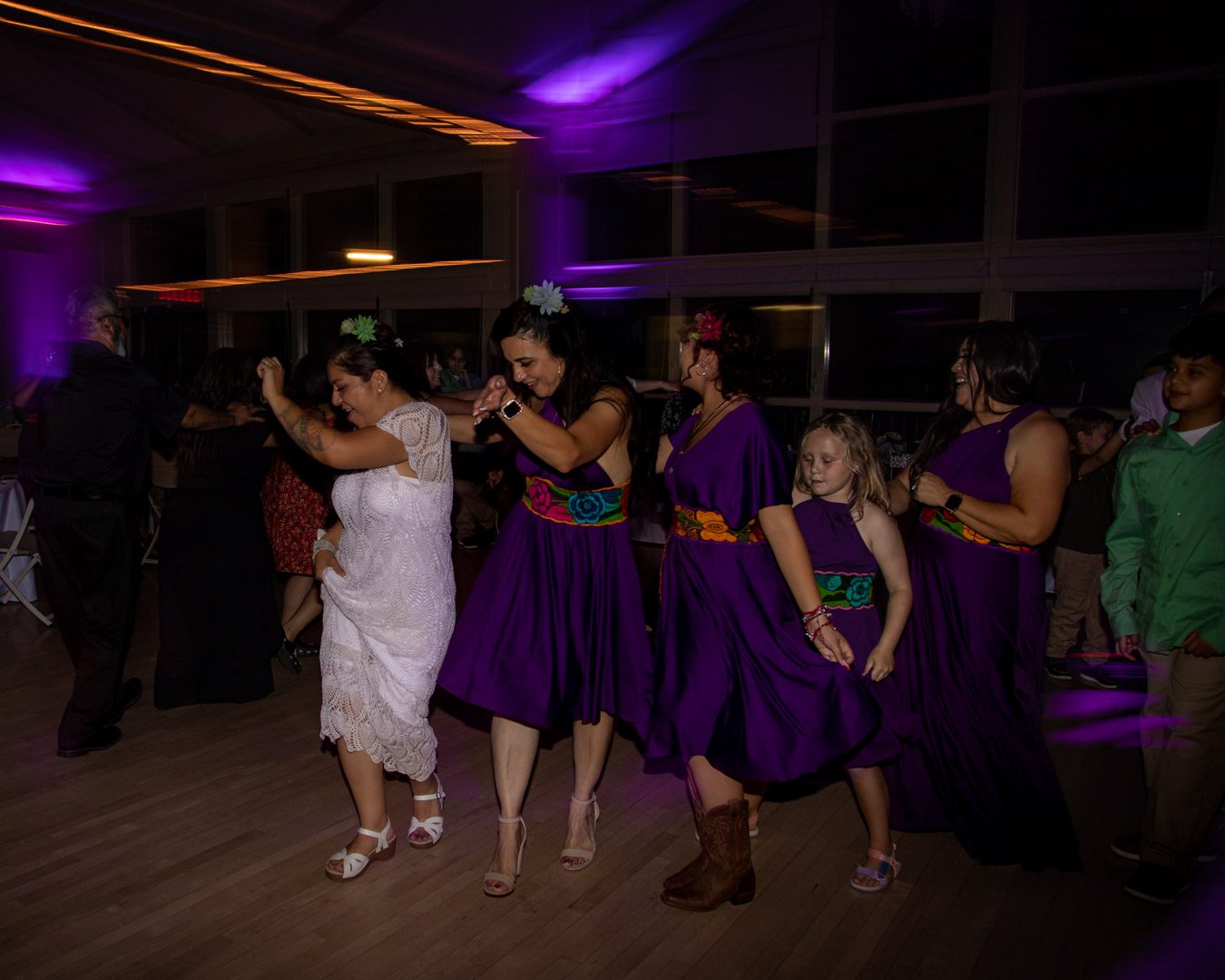 Bride and bridesmaids in purple dresses dancing in a line across the floor