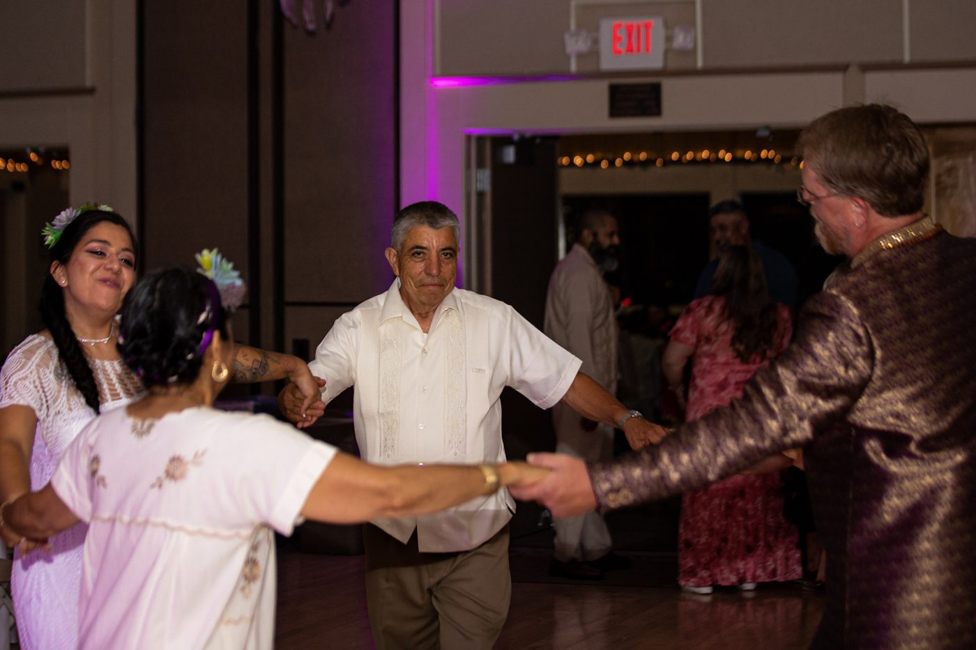 Guests holding hands in a circle dance under purple uplighting
