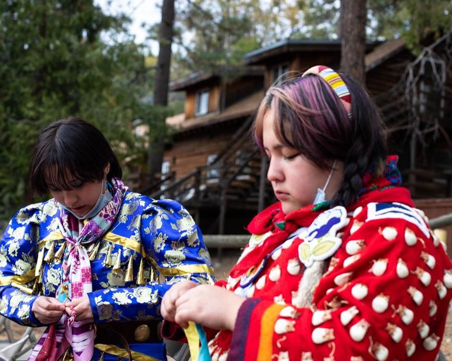 Two young women in traditional regalia preparing before an event
