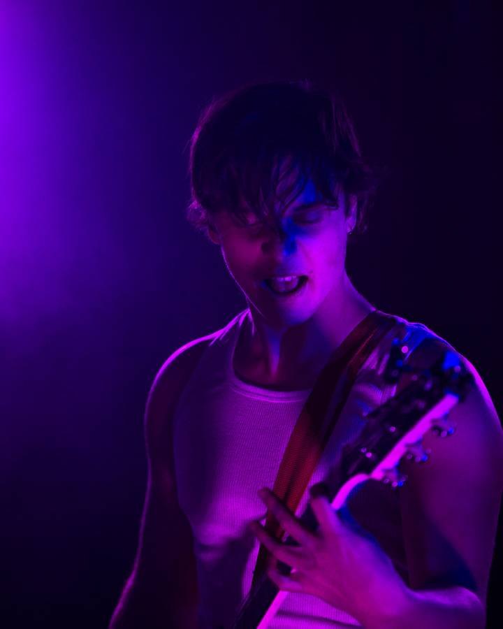 Guitarist performing under violet stage lighting