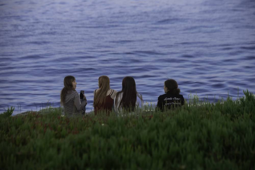 Four friends sitting on a bluff watching the ocean at dusk