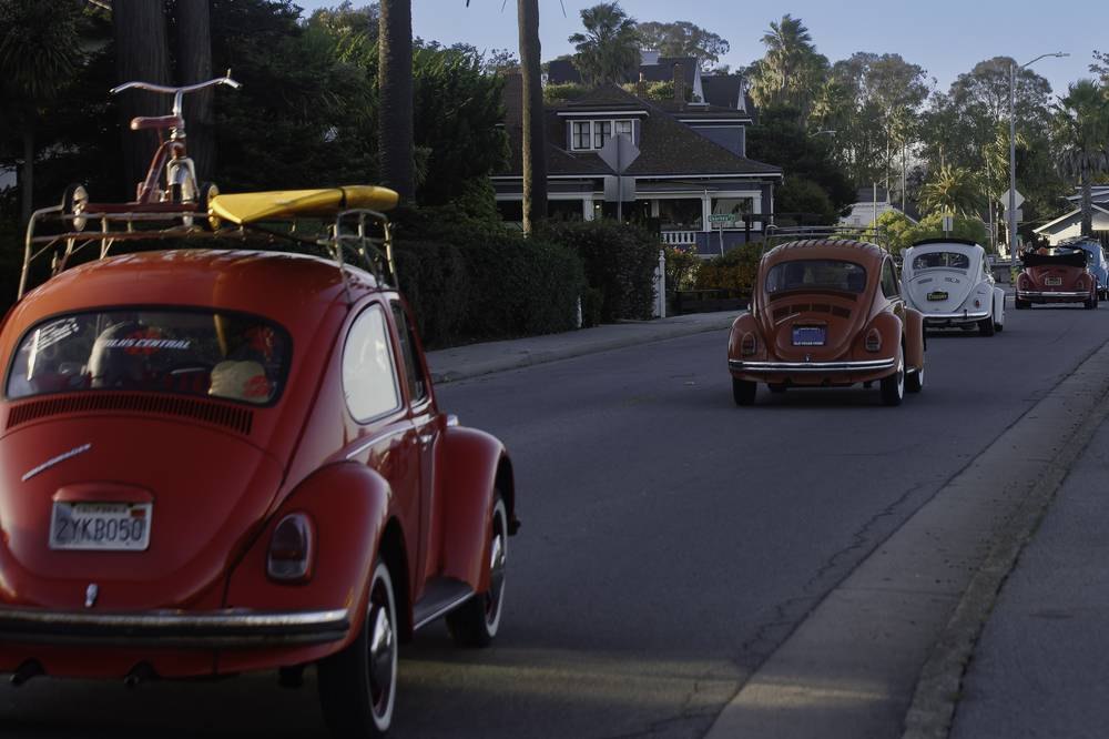 Vintage Volkswagen Beetles with roof racks driving down a Santa Cruz street