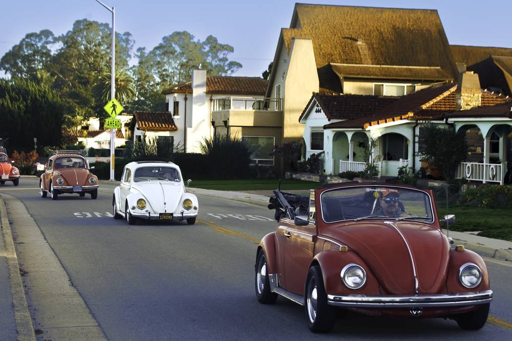 A row of vintage Volkswagen Beetles driving through a residential Santa Cruz street