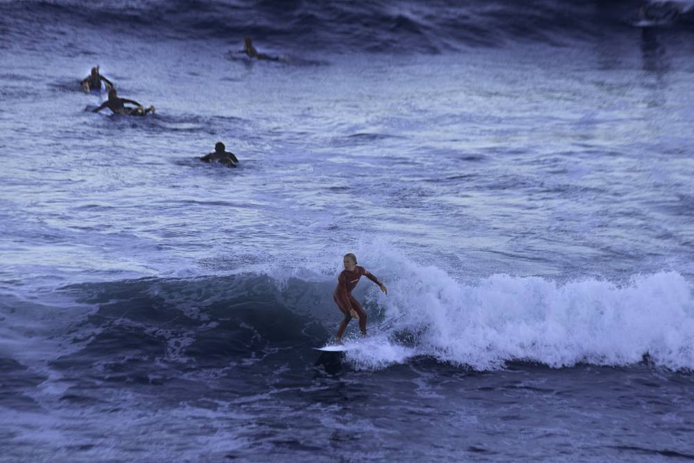 Surfer riding a wave at dusk with other surfers waiting nearby