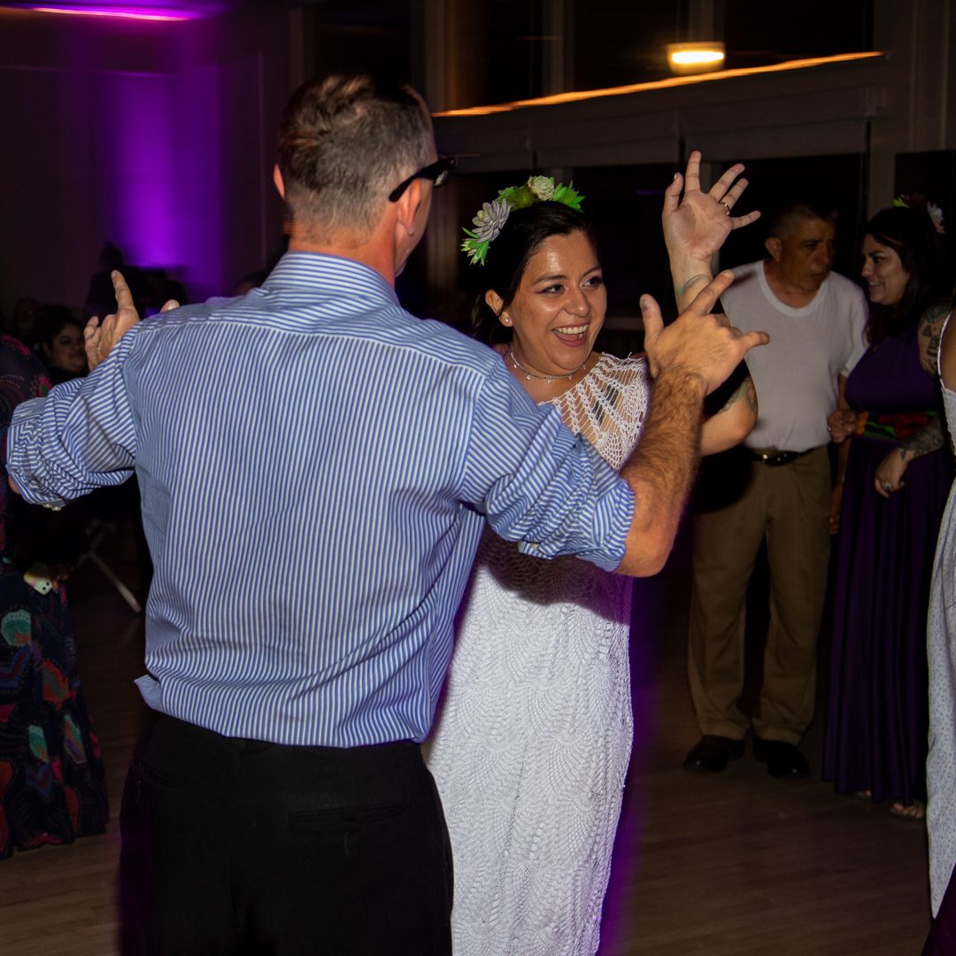 Bride laughing and dancing with a guest in a striped shirt