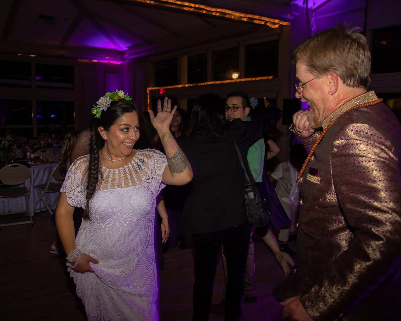 Bride waving with a big smile while the groom laughs beside her on the dance floor