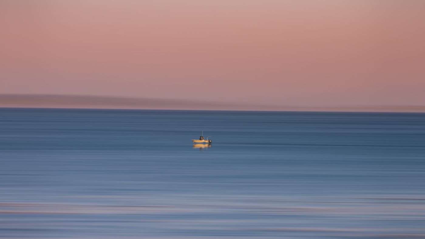 Small fishing boat on a long-exposure blue sea under a rose-colored sky