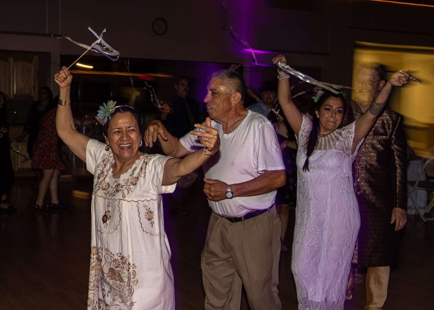 Guests dancing with ribbon wands raised, the bride and groom behind them