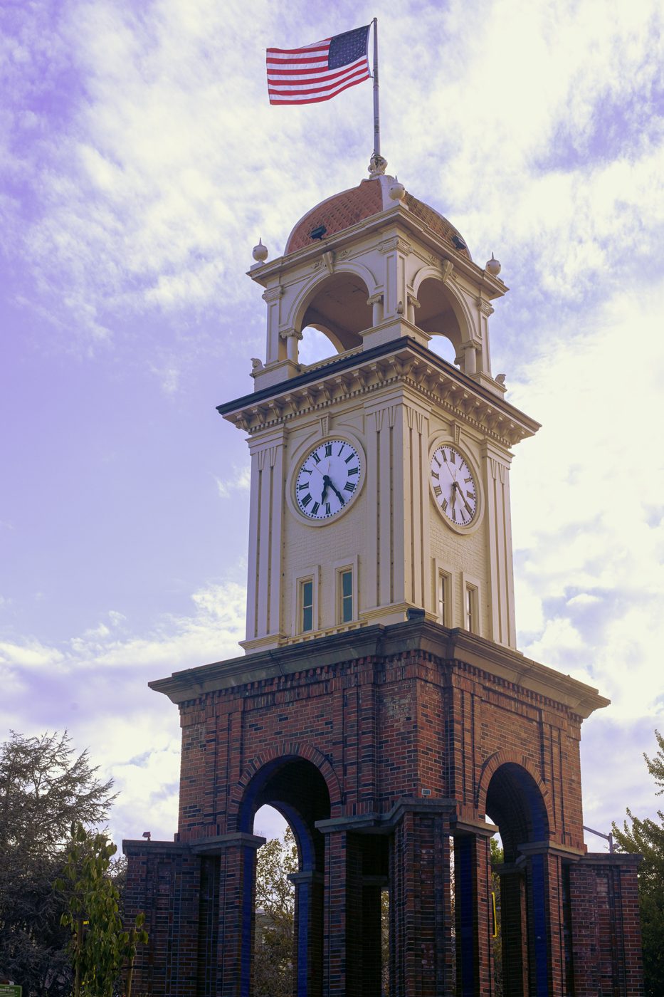 Brick and cream clock tower with an American flag against a purple-tinted sky